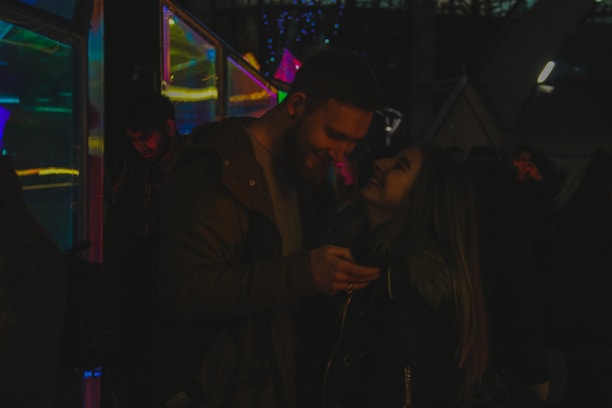 Smiling couple holding their instant photo strips, glowing under colorful event lights.