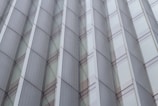 A modern architectural facade featuring repeating geometric patterns with glass panels and metallic frames. The design exhibits a symmetrical and orderly arrangement, creating a sense of depth and reflection.