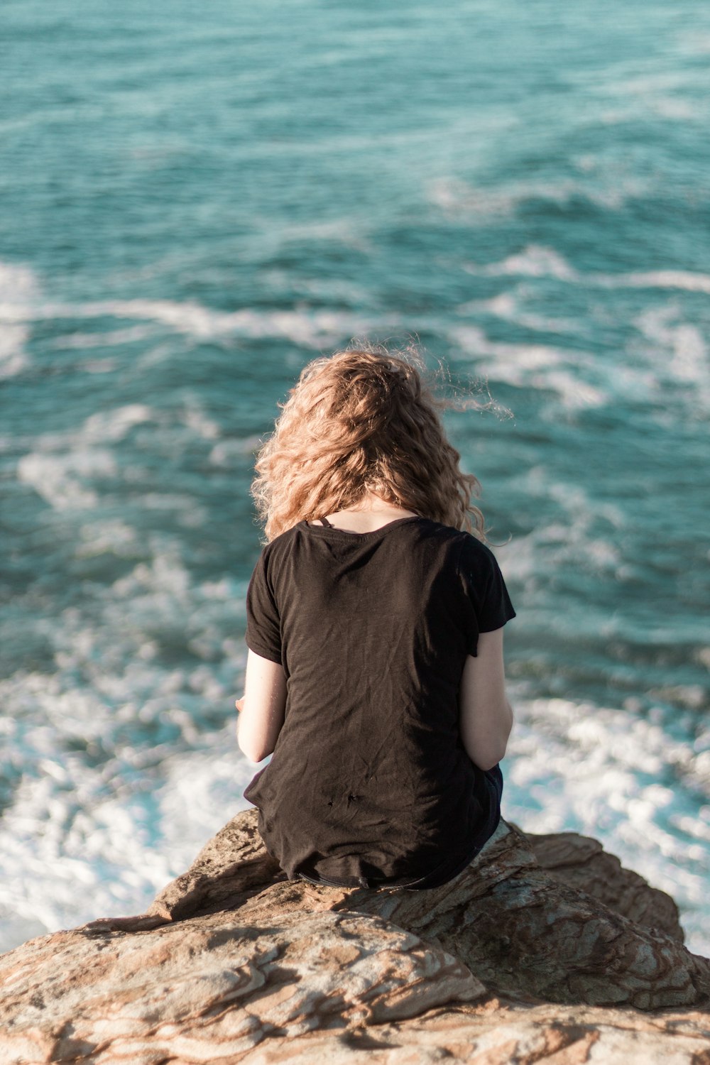 woman sitting on rock near body of water