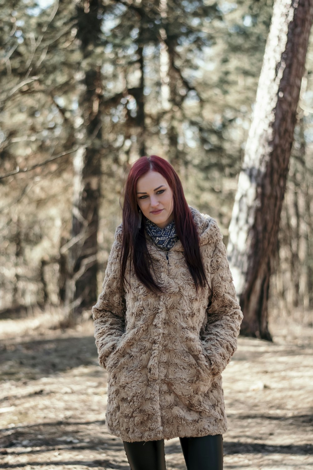 focus photography of woman wearing fur coat standing near trees during daytime