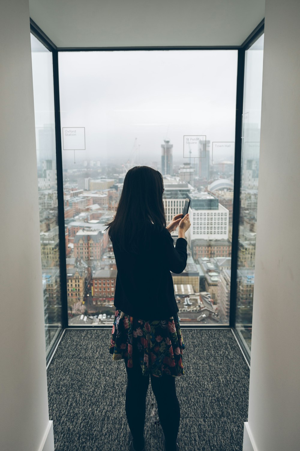 woman holding smartphone standing in front of window