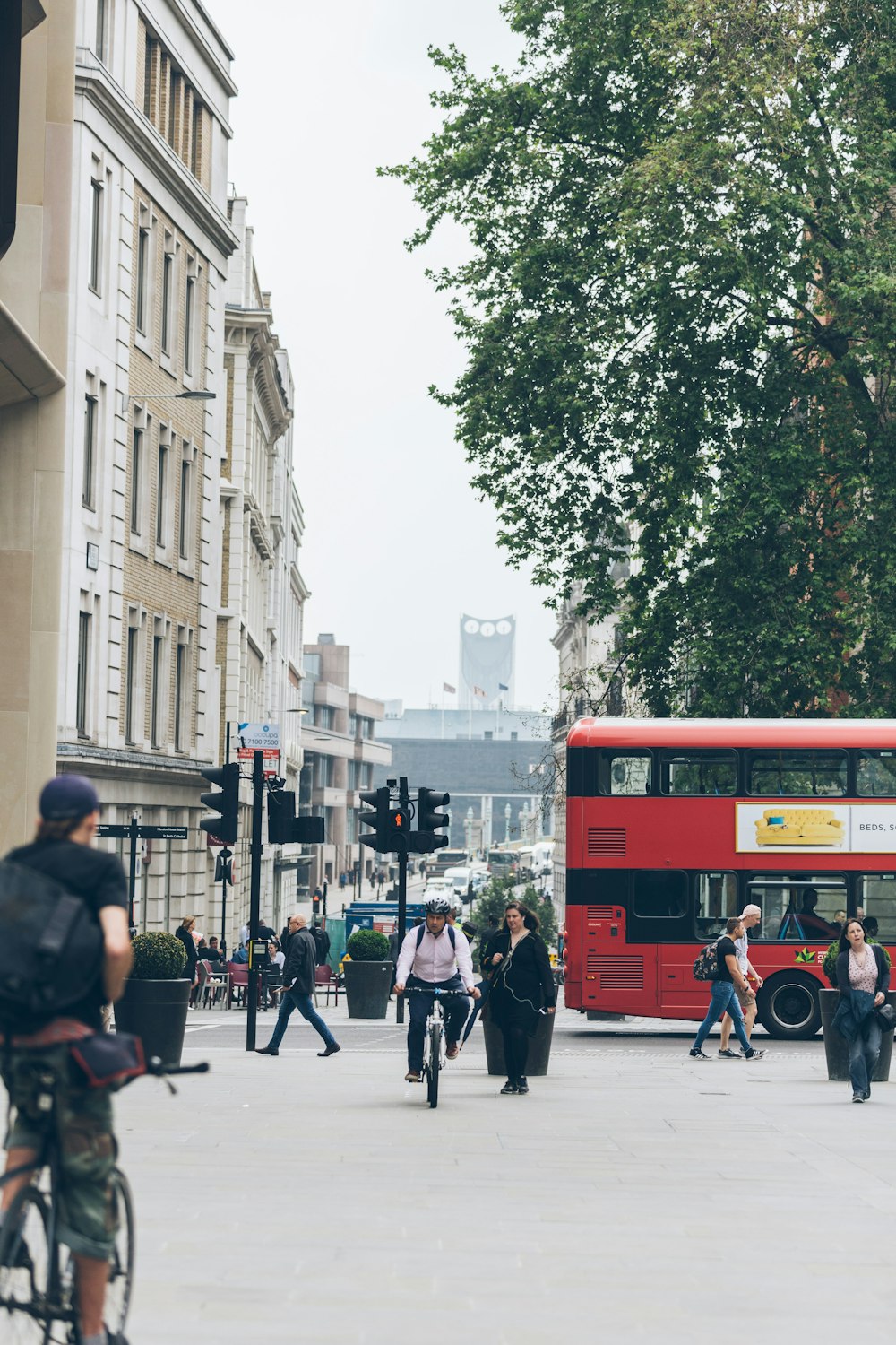 people riding bike and walking near red bus and white building during daytime