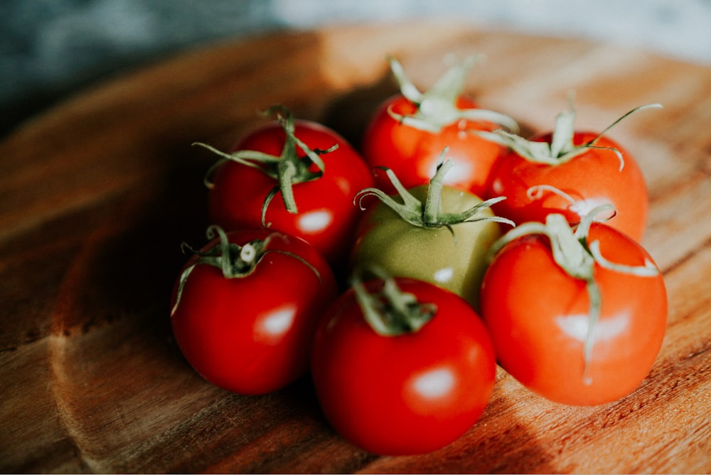 six red and one green tomatoes on brown wooden plate