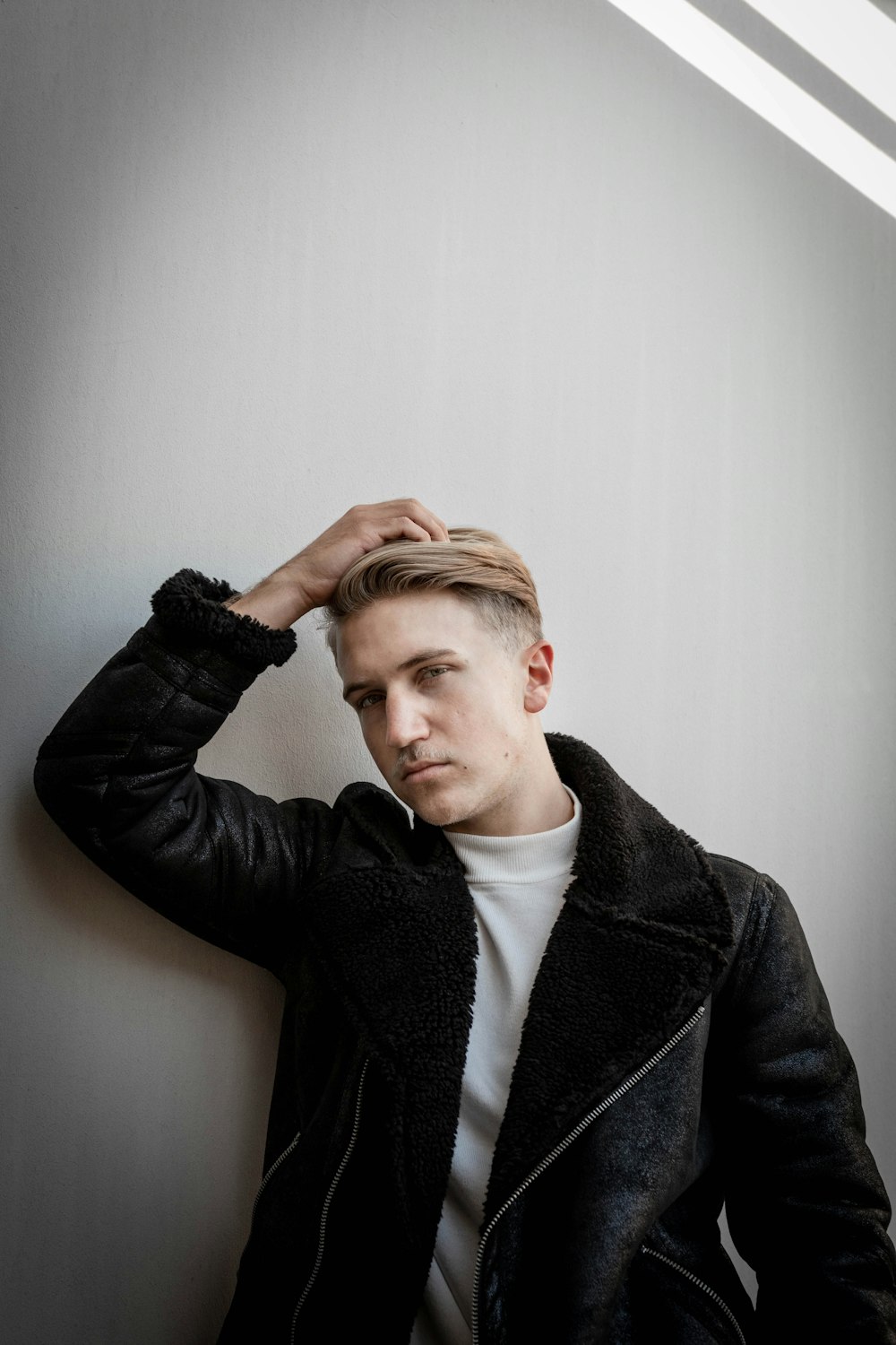 man leaning on wall while holding his hair