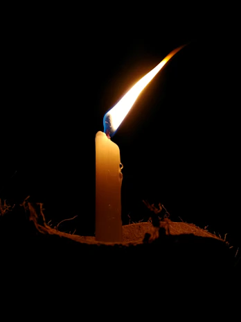 Elegant white candle with a flickering flame beside a small sprig of greenery on a light linen cloth.