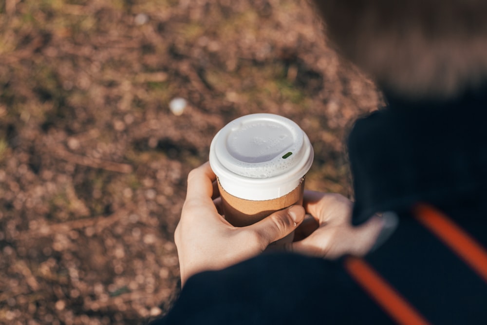 personne tenant une tasse blanche et brune