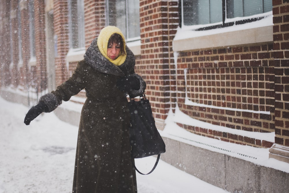 woman in black coat standing beside brick building