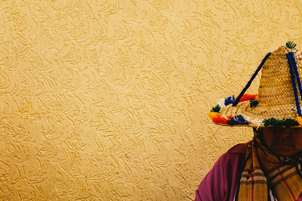 person wearing straw hat in front of yellow wall