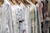 A row of intricately embroidered blouses hanging on wooden hangers. Each garment features unique patterns in various colors such as blue, red, and green, set against a predominantly white fabric. The embroidery includes floral and geometric designs.
