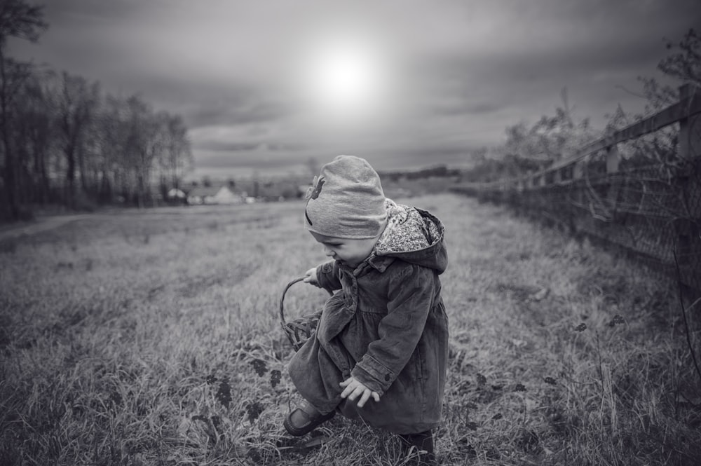 grayscale photo of baby standing in the middle ok grass field