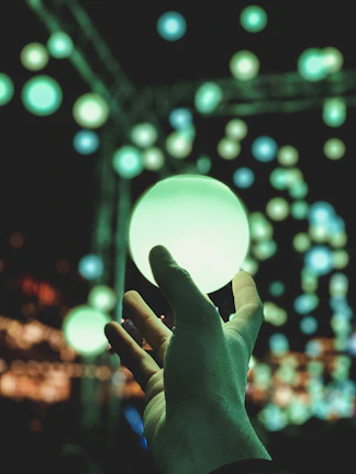 Close-up of a hand reaching toward a shimmering, translucent orb of light hovering in darkness.