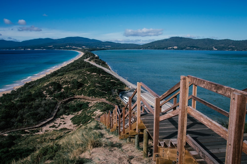 brown wooden pathway over the valley surrounded by blue sea during daytime