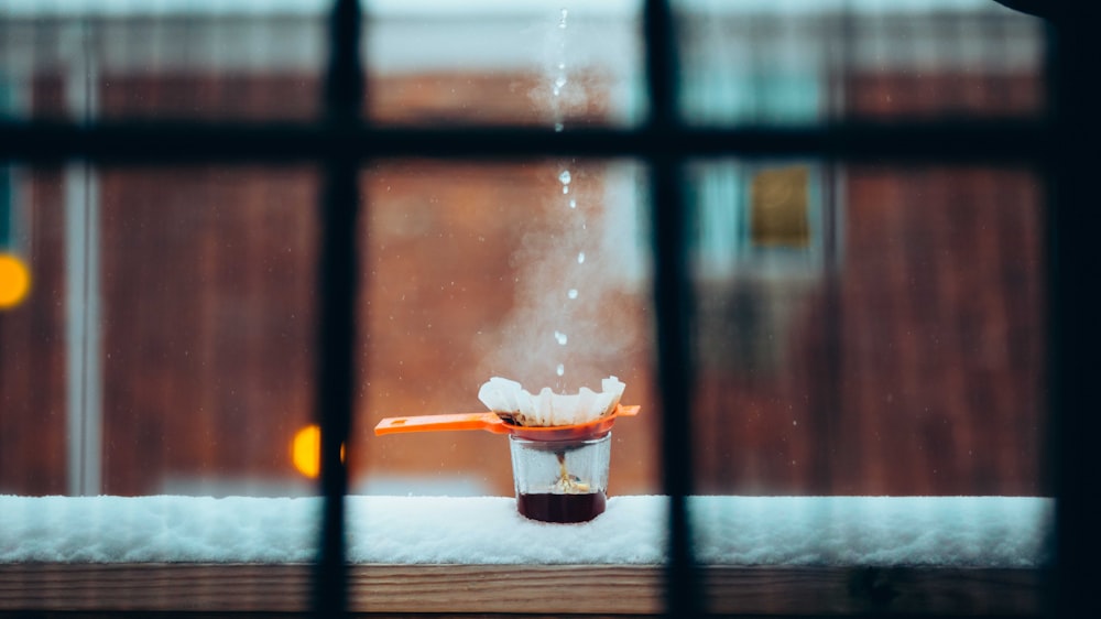 a cup filled with liquid sitting on top of a window sill