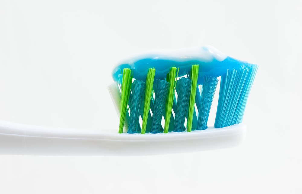 Escova de dentes branca, azul e verde com pasta de dentes azul