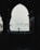 A silhouette of a camera on a tripod is framed by an archway, with a misty waterfront and distant buildings in the background. The scene is moody and atmospheric, with minimal visibility due to the fog.