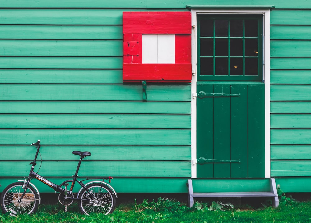 black folding bicycle leaning beside green house