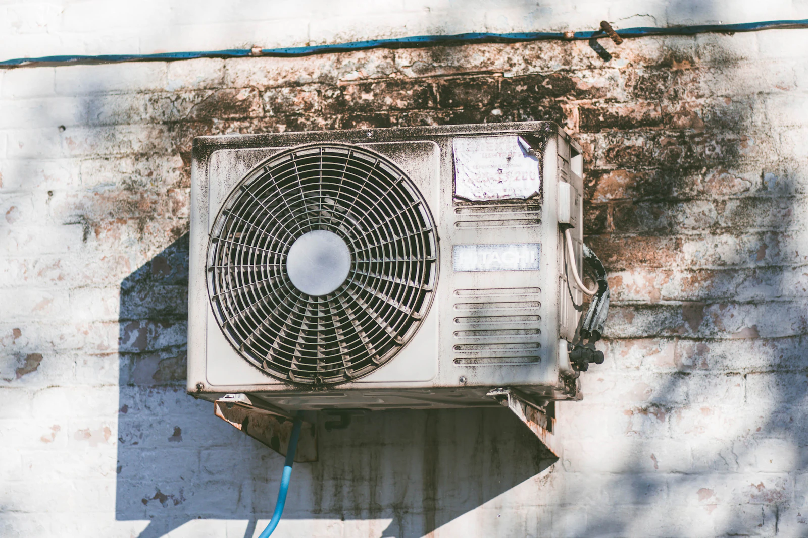 An outdoor air-conditioning condenser unit mounted on the exterior wall of a home in the Gulf heat