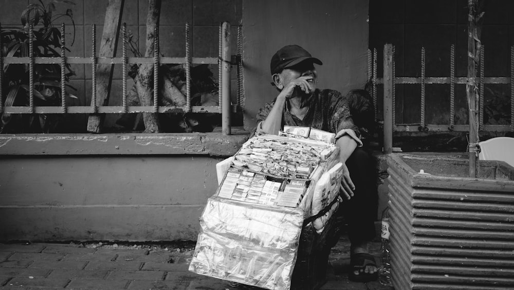 grayscale photography of man sitting beside fence