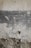 A textured, weathered wall with layers of peeling paint, revealing different shades of grey and beige beneath. The surface appears rough, with visible cracks and irregular patterns. There is a section of exposed concrete at the bottom, adding to the rustic and aged appearance.