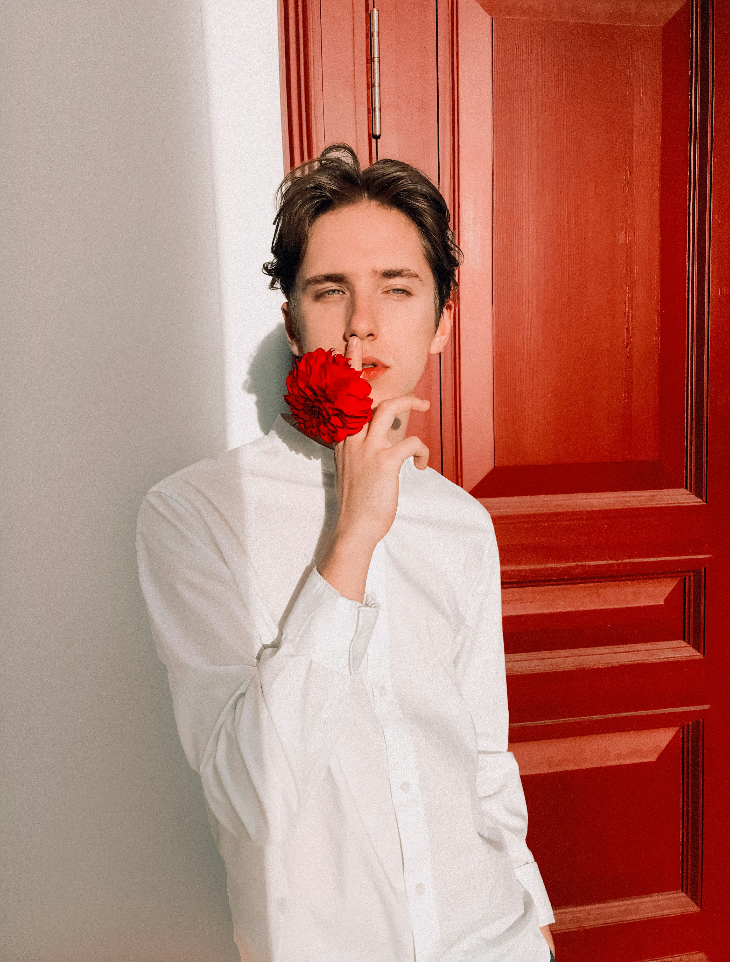 man standing beside door while holding red flower