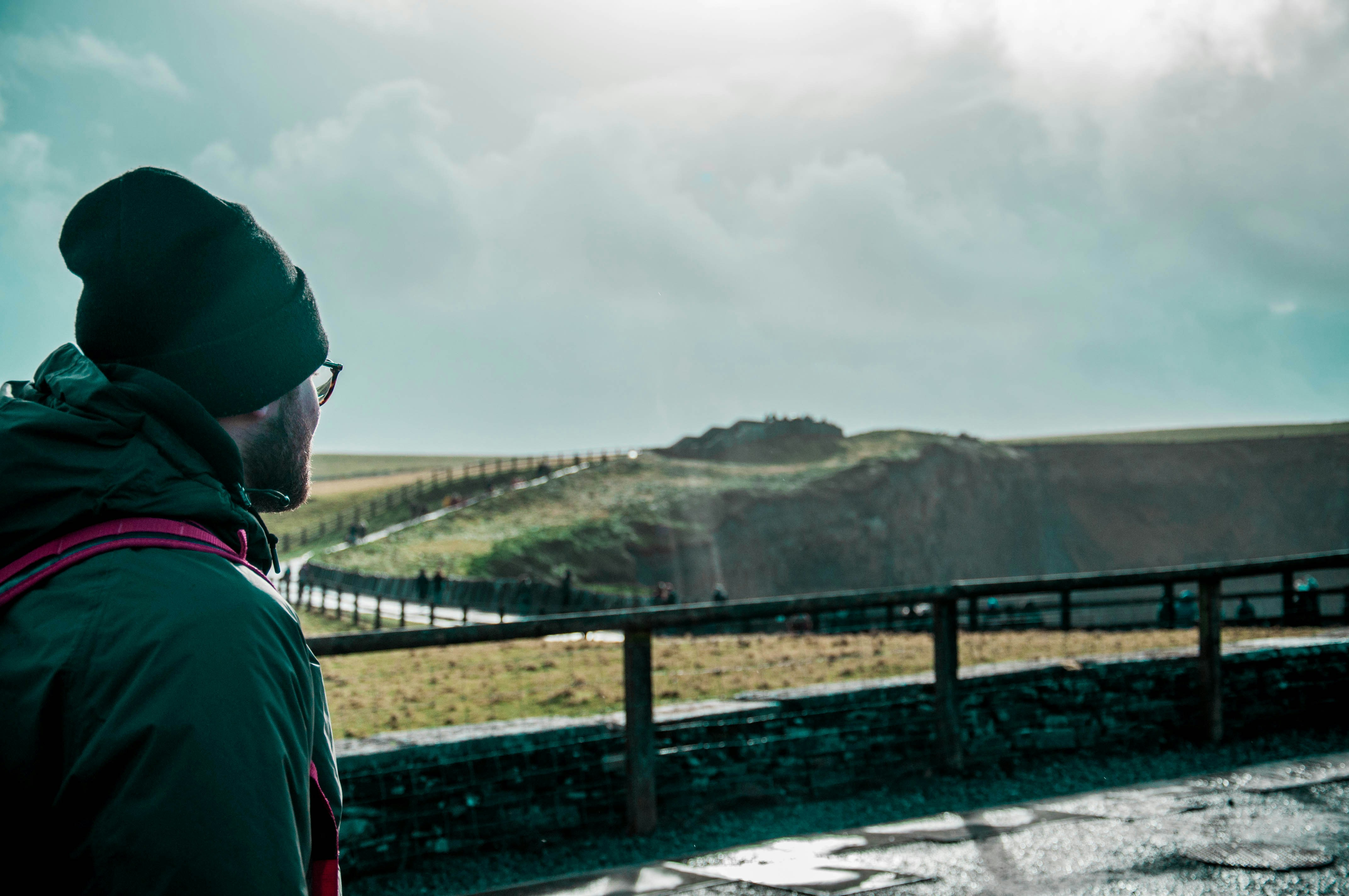 man in grey jacket stands facing green grass covered hill