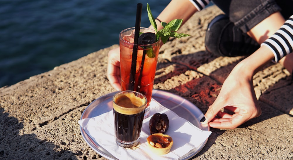 person putting glass filled with beverages on plate