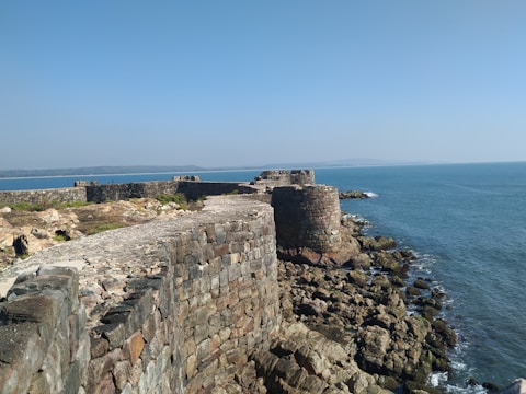 A robust sea defense wall extending along a rocky shoreline under a clear sky.