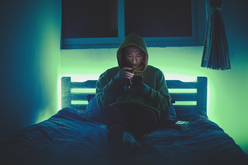 man sitting on bed while using smartphone