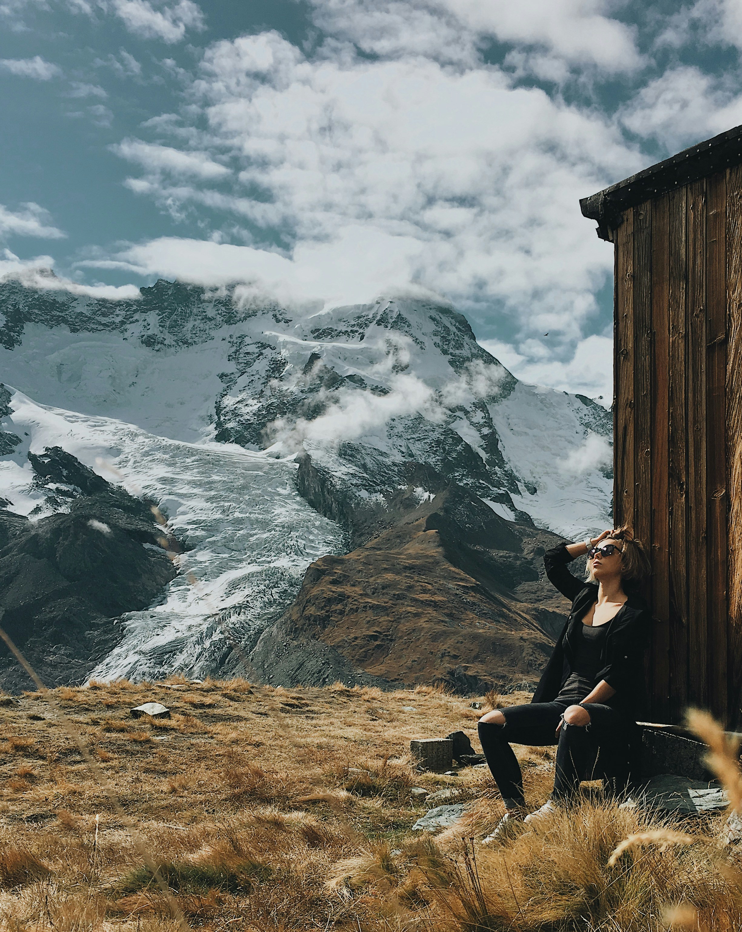 femme portant une chemise noire assise sur un rocher avec vue sur une montagne enneigée