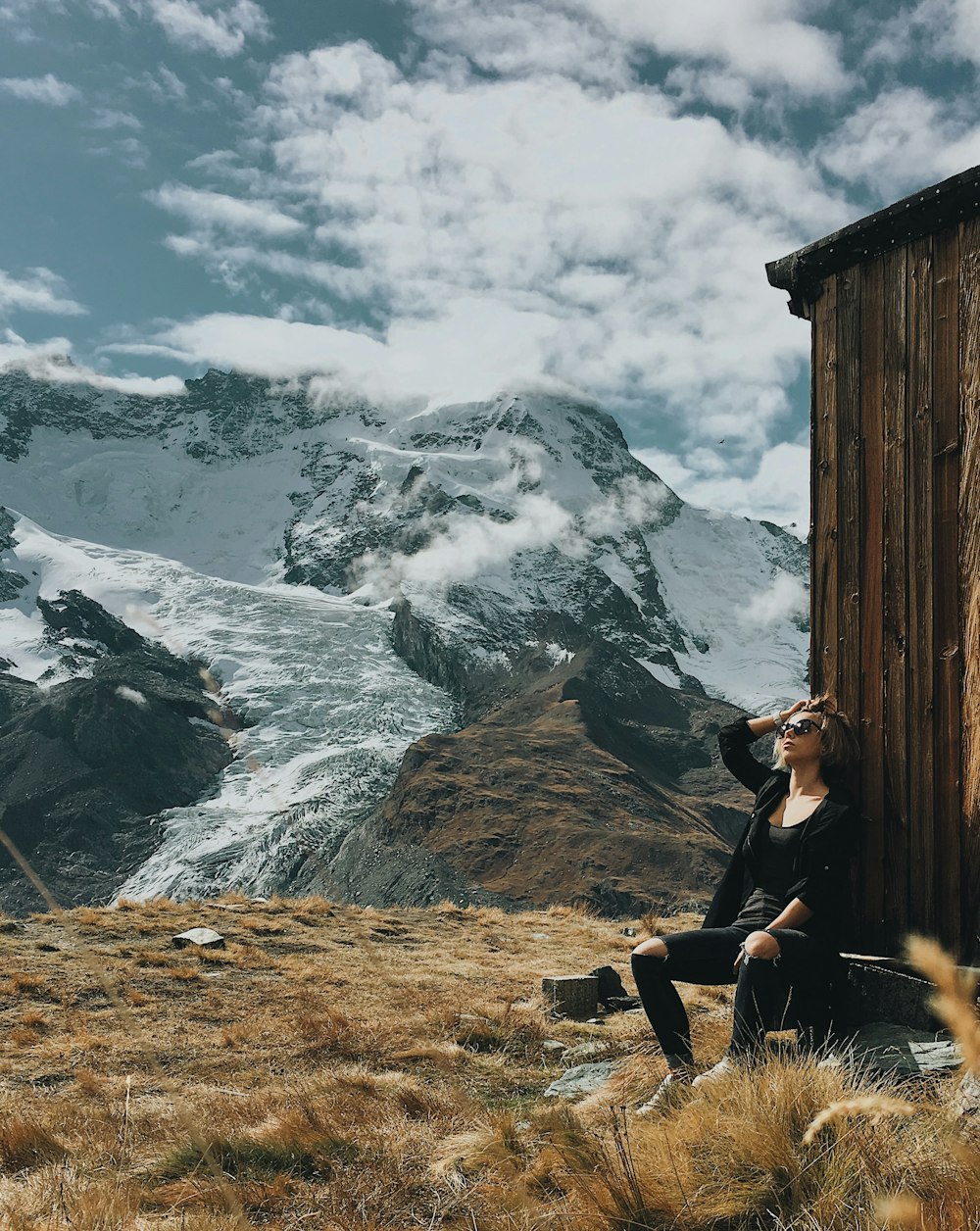 woman wearing black shirt sitting on rock with view of snow capped mountain