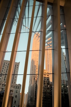Glass windows reflect a cityscape featuring tall skyscrapers under a soft, warm light with architectural elements casting shadows.