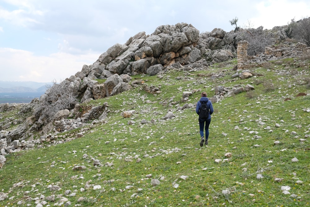 man in black jacket walking towards rocky hill