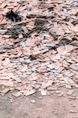 A large pile of broken and scattered tiles lies on the ground, covering a significant area. The tiles are primarily beige with some blue and other colored edges. Among the tiles, there are small remnants of other materials and debris.