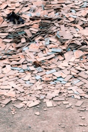 A large pile of broken and scattered tiles lies on the ground, covering a significant area. The tiles are primarily beige with some blue and other colored edges. Among the tiles, there are small remnants of other materials and debris.