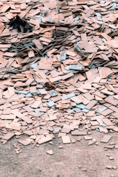 A large pile of broken and scattered tiles lies on the ground, covering a significant area. The tiles are primarily beige with some blue and other colored edges. Among the tiles, there are small remnants of other materials and debris.