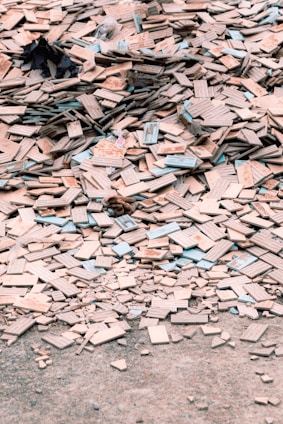 A large pile of broken and scattered tiles lies on the ground, covering a significant area. The tiles are primarily beige with some blue and other colored edges. Among the tiles, there are small remnants of other materials and debris.