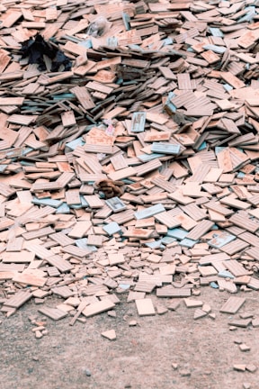 A large pile of broken and scattered tiles lies on the ground, covering a significant area. The tiles are primarily beige with some blue and other colored edges. Among the tiles, there are small remnants of other materials and debris.