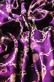 Richly detailed fabric with intricate patterns of chains, tassels, and other ornamental designs. The fabric is draped elegantly, showcasing its shiny texture and elaborate motifs.