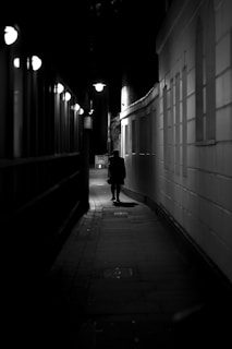 A shadowy figure walking through narrow streets of Montpellier under streetlights.