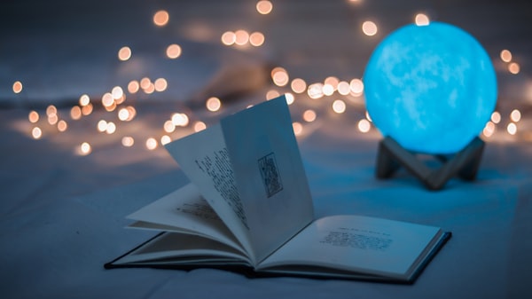 An open book with several pages sticking up and a blue crystal ball, framed with fairy lightsd.