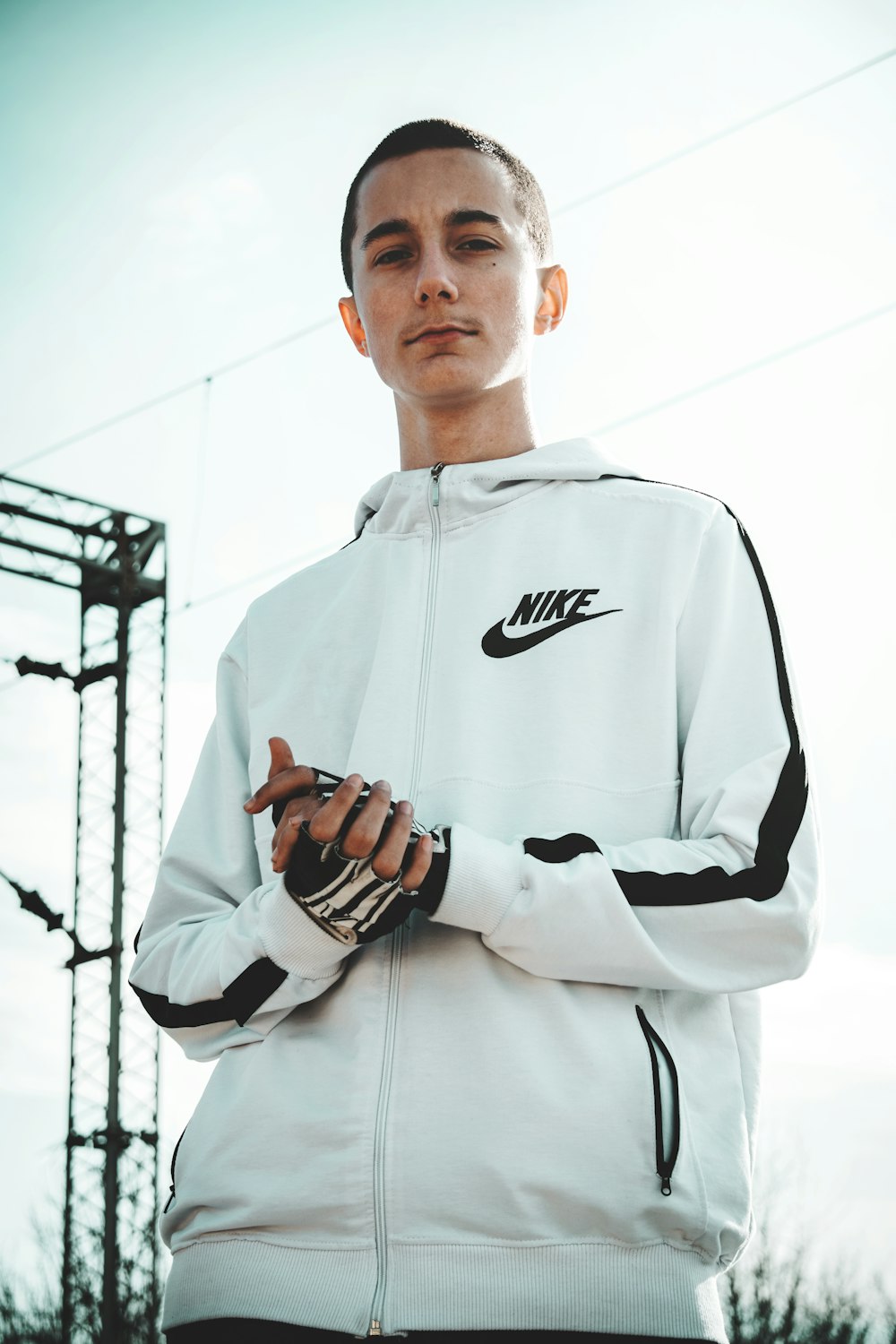 man wearing white and black full-zip Nike hoodie standing across electric cable wires