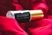 A bottle of 'Midnight Eau De Parfum' is resting on a rich, red fabric. The bottle features a sleek black and gold design, creating a luxurious and elegant aesthetic.