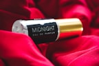 A bottle of 'Midnight Eau De Parfum' is resting on a rich, red fabric. The bottle features a sleek black and gold design, creating a luxurious and elegant aesthetic.