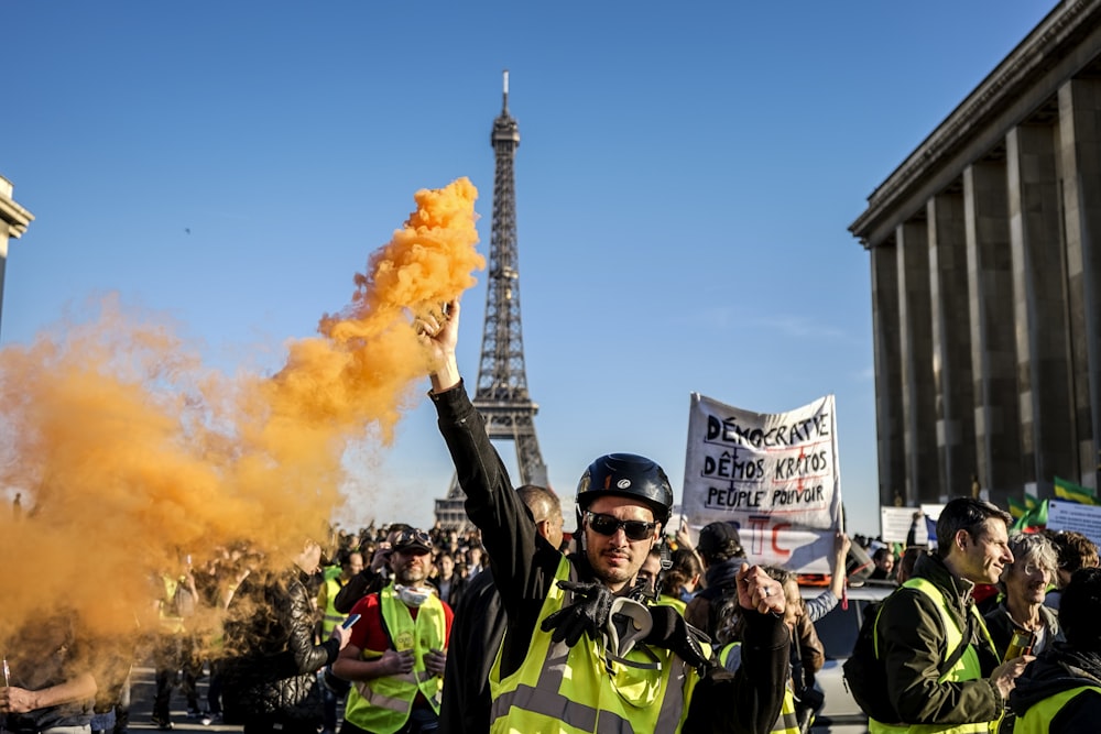 昼間のパリに立ってオレンジ色の煙を上げる男