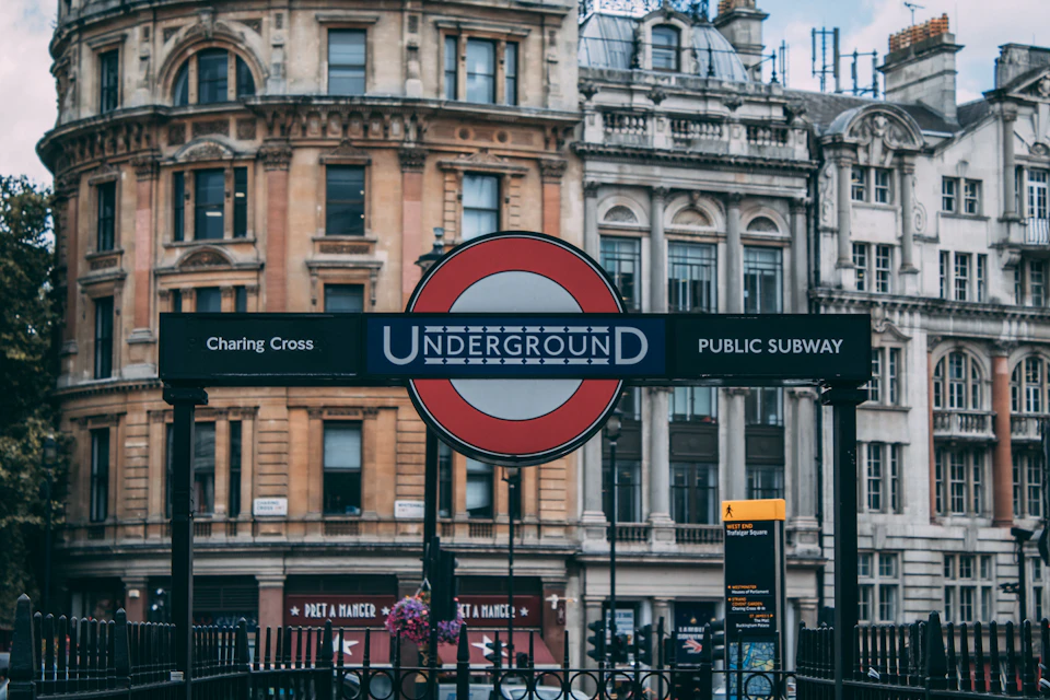 Large red and white "Underground" sign at crosswalk with two buildings nearby pedestrians