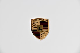 A shield-shaped emblem with a gold outline and intricate details, featuring a prancing horse and a combination of black and red stripes.