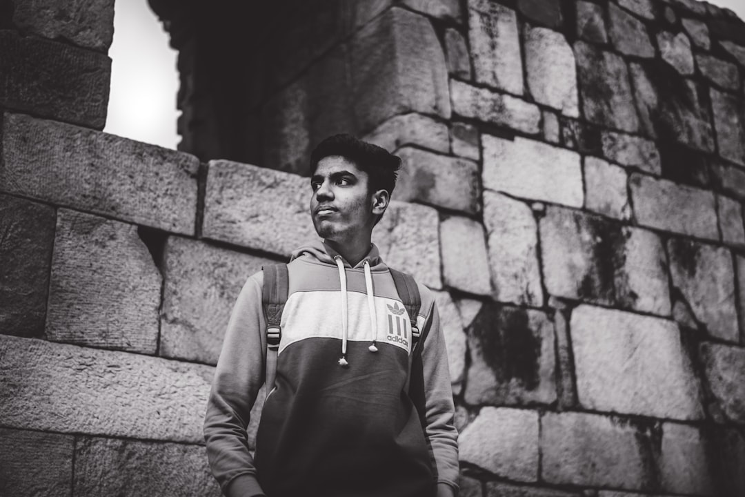 grayscale photography of man standing near brick wall