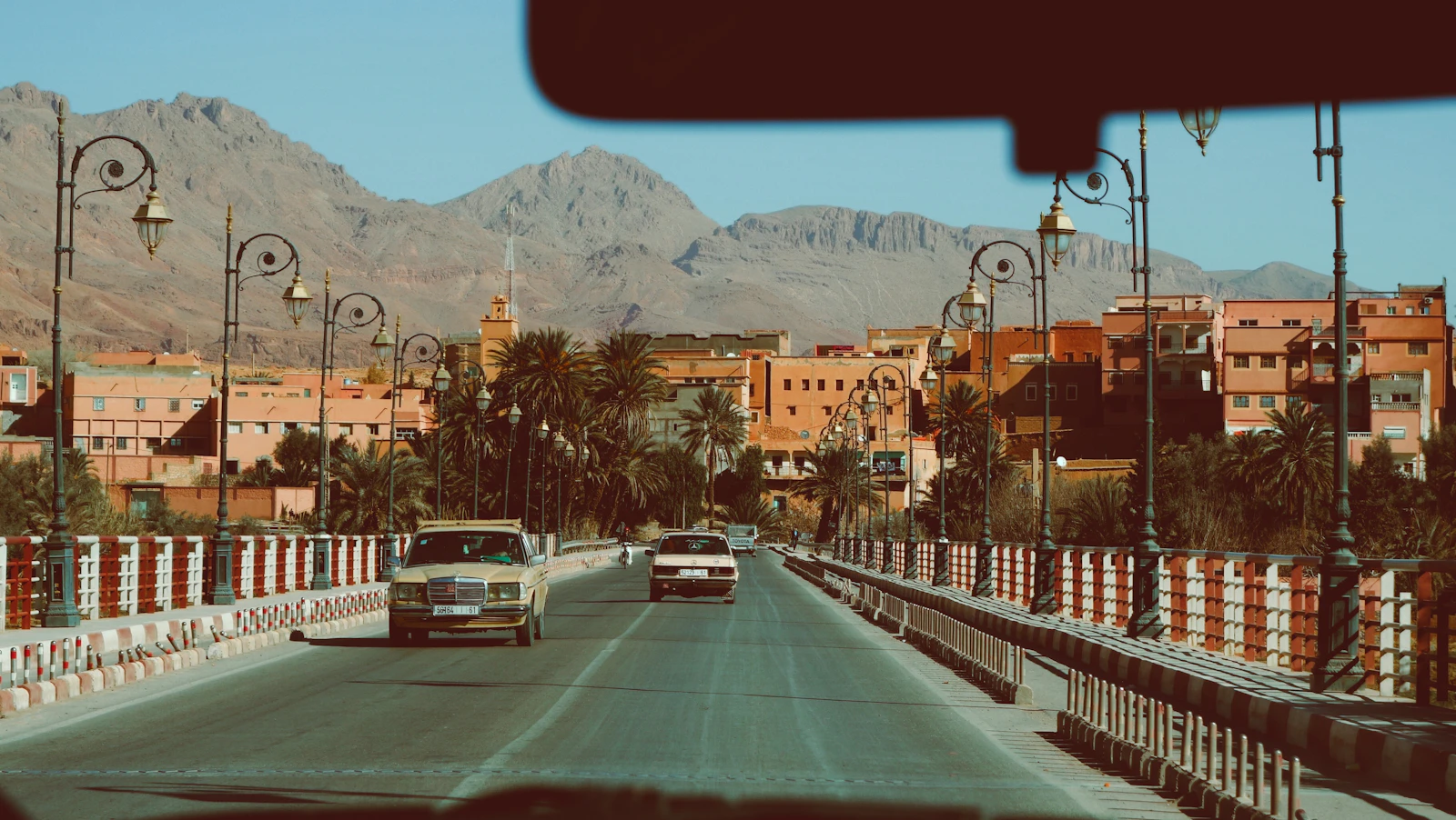 A white car travelling on an open road below Moroccan mountains