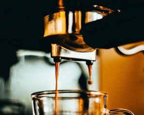 Hands pouring freshly brewed coffee into a clear glass cup capturing golden hues