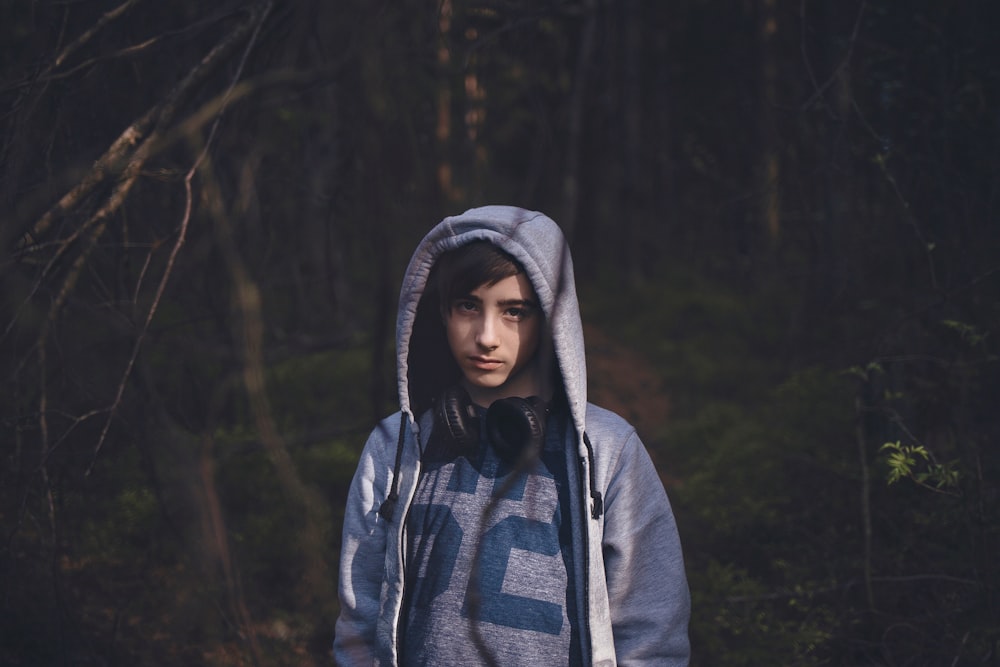 uomo che indossa giacca con cappuccio blu in piedi sulla foresta